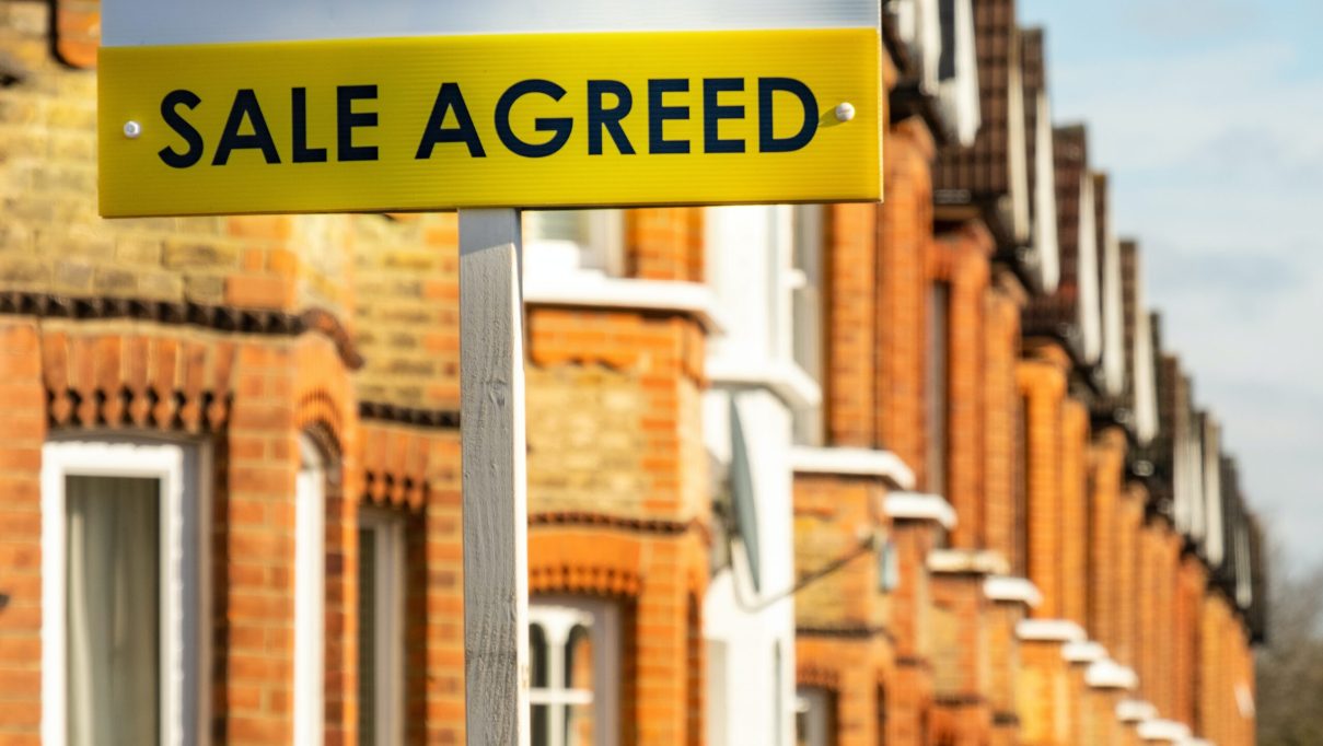Estate agent 'Sale Agreed' sign on street of red brick houses